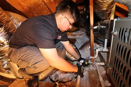 Extreme Comfort AC technician installing a Drain Guard device on an HVAC drain line in an attic.